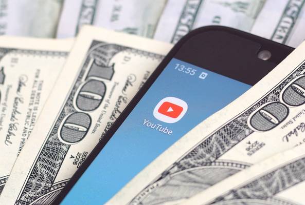 Smartphone showing YouTube app surrounded by hundred-dollar bills, symbolizing earnings