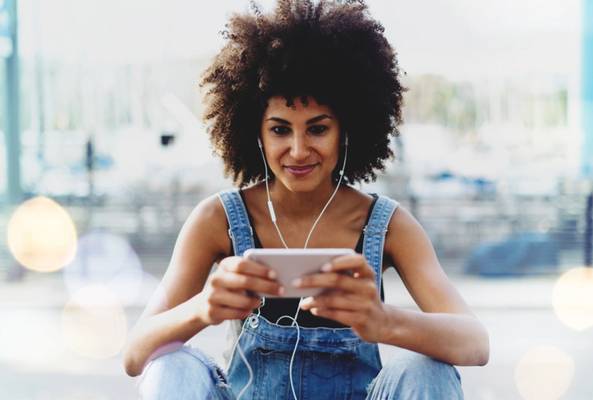 Young woman with headphones using smartphone outdoors, casual urban setting background