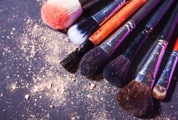Set of makeup brushes with powder residue on a dark textured surface.