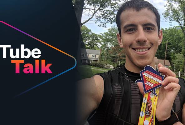 Young man holding a 2018 superhero race medal outdoors, Tube Talk logo beside him