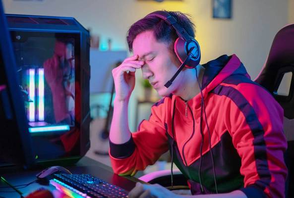 Frustrated gamer wearing headset resting forehead in front of gaming PC and keyboard.