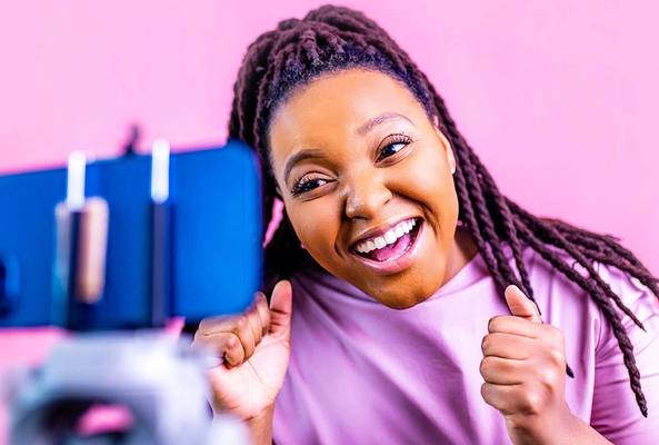 Smiling woman recording video with smartphone on tripod against pink background