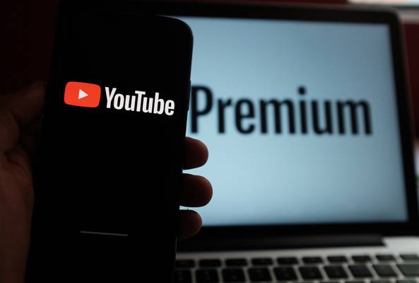 YouTube logo on smartphone with blurred YouTube Premium on laptop screen in background
