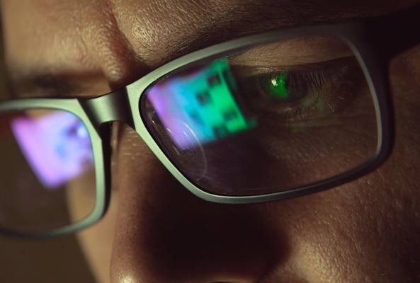 Close-up of man wearing glasses with digital screen reflection on lenses at night