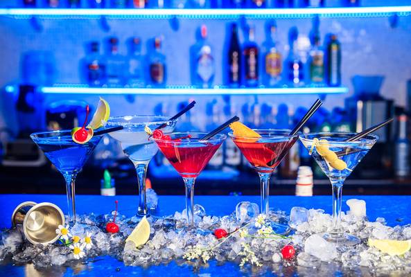 Colorful cocktails garnished with fruit and cherries on ice at a modern bar setting