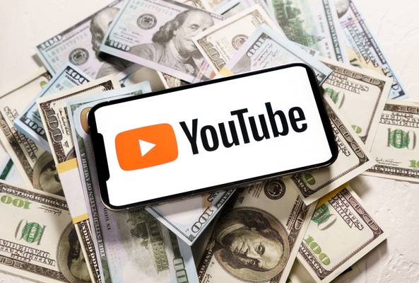 Smartphone displaying YouTube logo on a pile of US dollar bills, symbolizing earnings.
