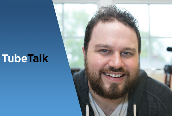 Man smiling in front of a camera with TubeTalk logo on a blue background panel